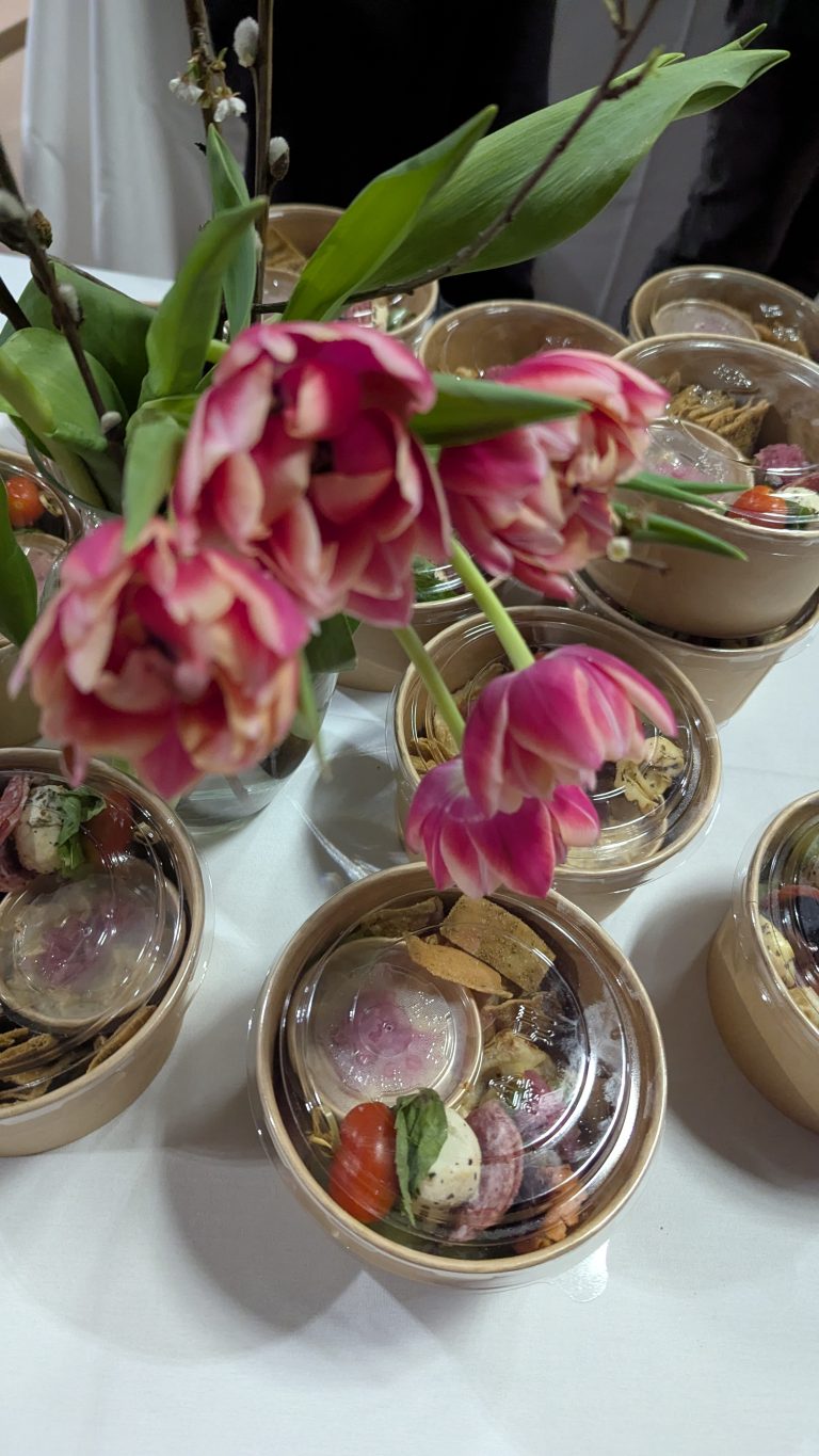 Pink tulips in a vase sit on a table surrounded by small bowls filled with assorted desserts, including strawberries, herbs, and decorative elements.